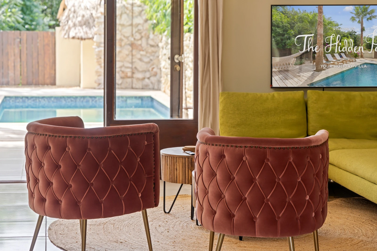 Living room with pink armchairs, green sofa and a view of the pool